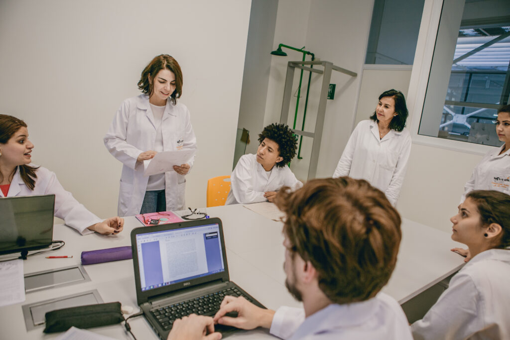 A group of students in lab coats sitting and listening to their teacher