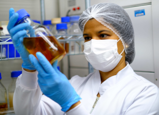 Woman in protective clothes looking at a liquid in a glass.