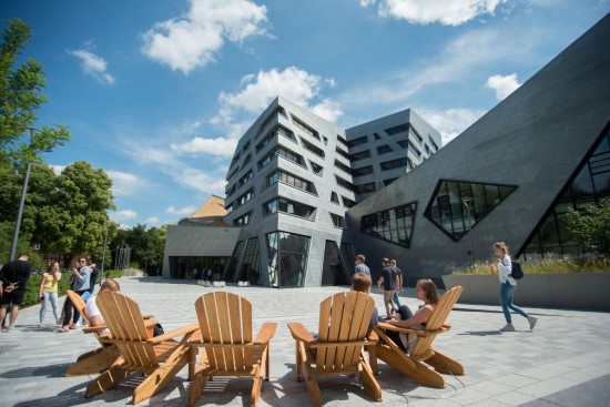 An outdoor view of the central campus building at Leuphana University. Blue sky, a modern campus building and a square with wooden armchairs
