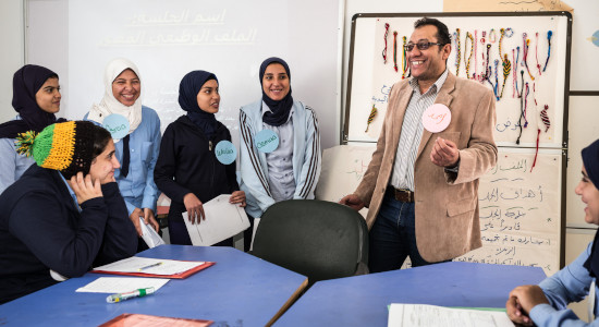 smiling man explaing something to a group of smiling female students.