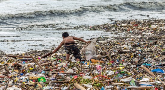 A man collecting plastic waste in a pile of garbage in the sea