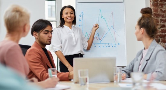 Portrait of mixed race businesswoman standing by whiteboard and giving presentation to colleagues during meeting in conference room.