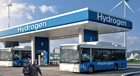 Two people walking towards a hydrogen station with two parked busses.