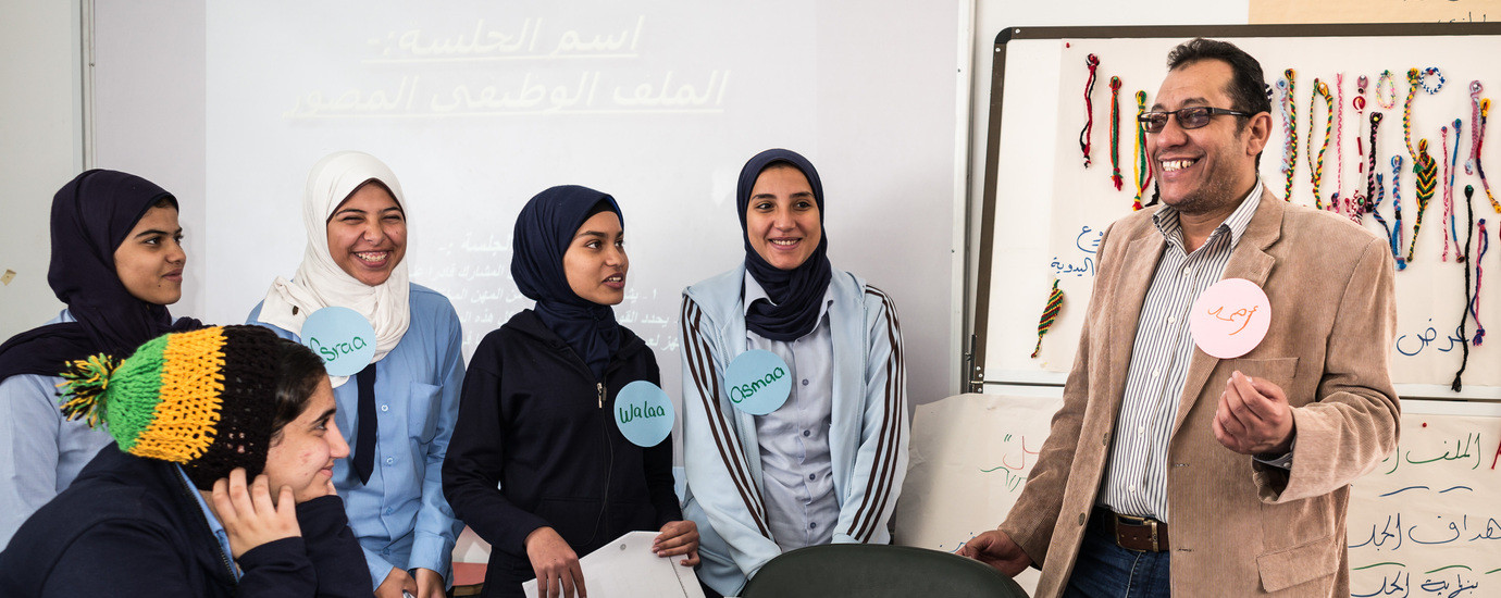 Smiling man explaing something to a group of female smiling students.