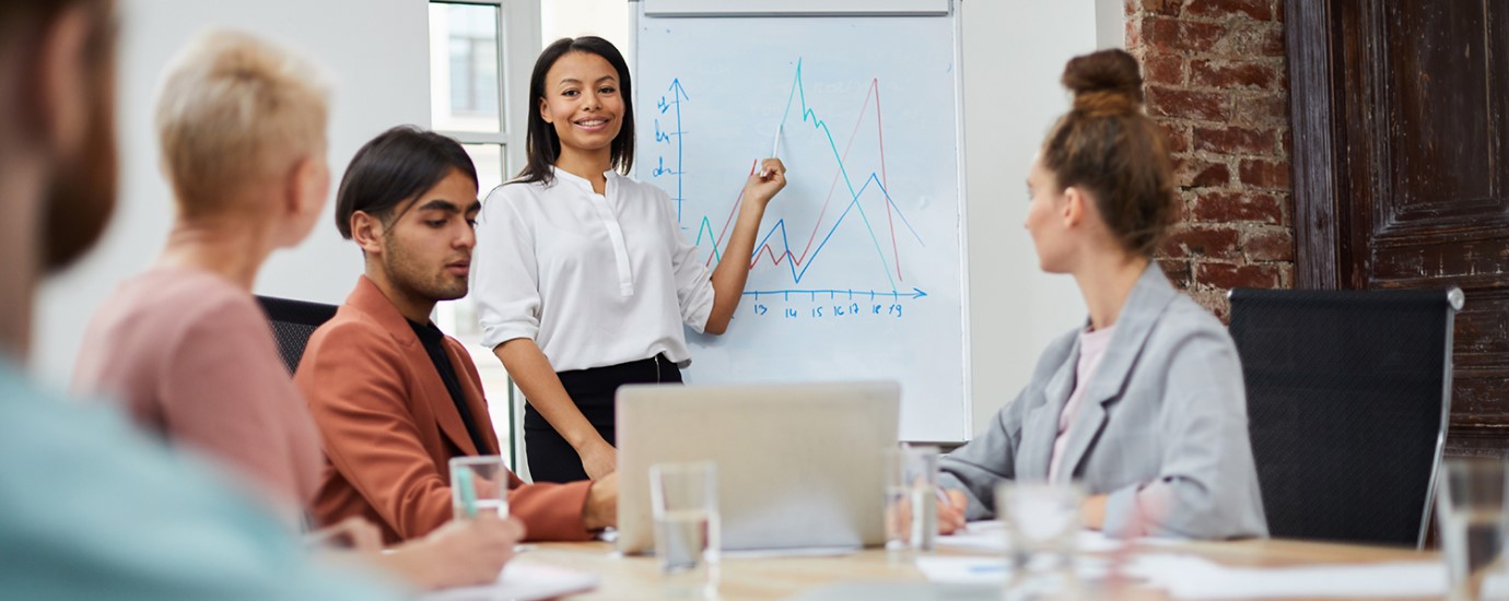 Portrait of businesswoman standing by whiteboard and giving presentation to colleagues during meeting in conference room