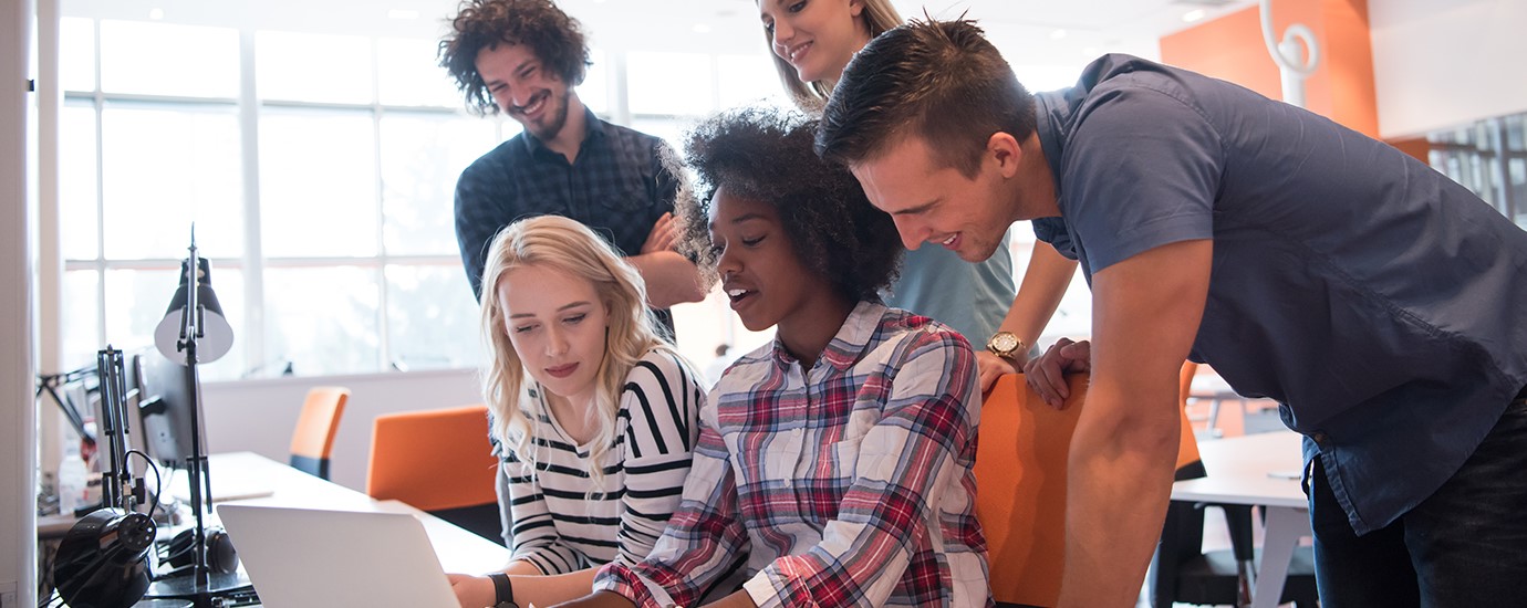 group of five young people looking at one lap top