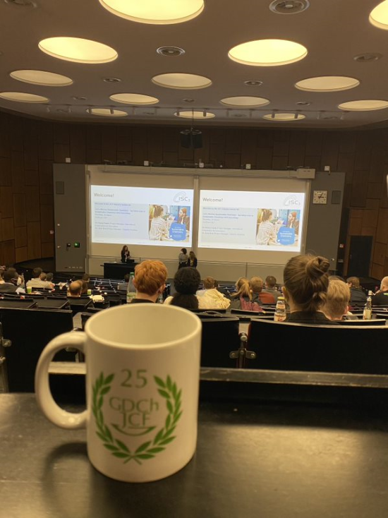  A cup showing the anniversary logo of the young chemists forum in front of a lecture hall during a presentation by ISC3 