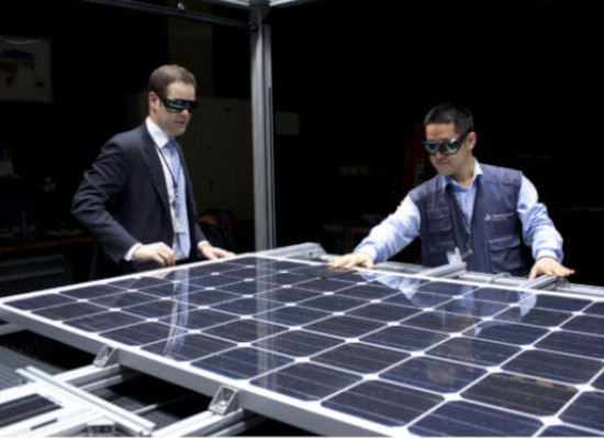 Twwo men with safety goggles examining a solar panel in an indoor setting