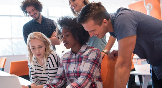 group of five young people looking at one lap top