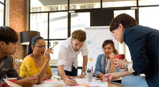 group of five working people around a table drawing on a paper and brainstorming.