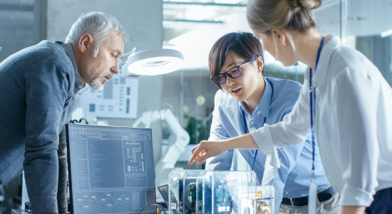 Team of Computer Engineers Choose Printed Circuit Boards to Work with, Computer Shows Programming in Progress. In The Background Technologically Advanced Scientific Research Center.