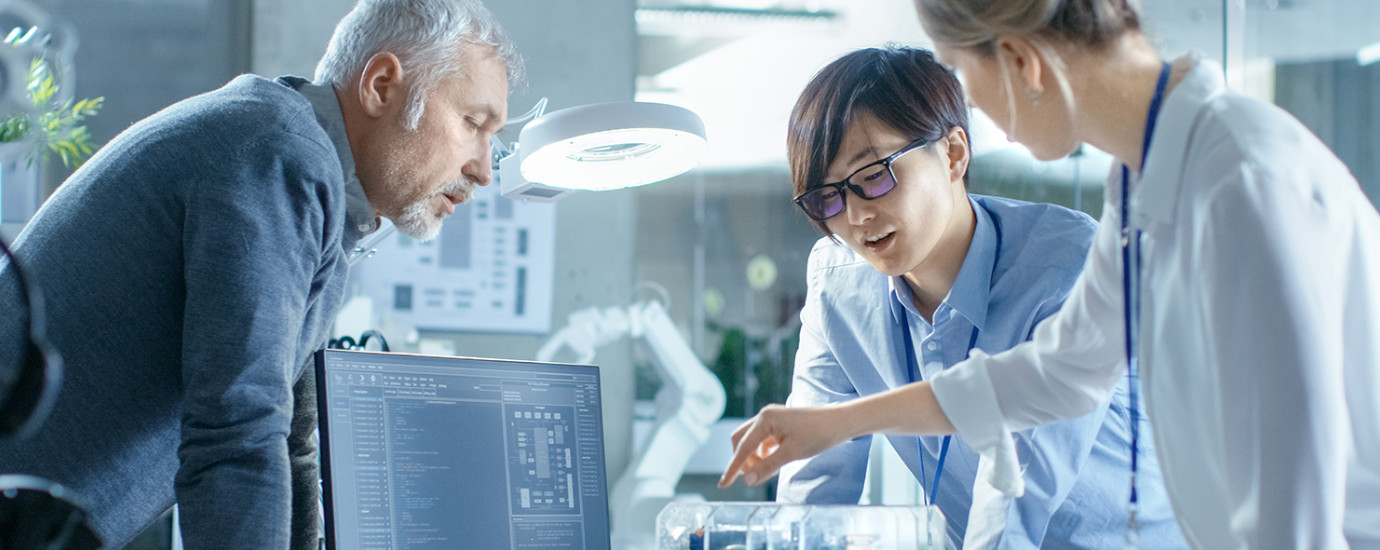 Team of Computer Engineers Choose Printed Circuit Boards to Work with, Computer Shows Programming in Progress. In The Background Technologically Advanced Scientific Research Center.