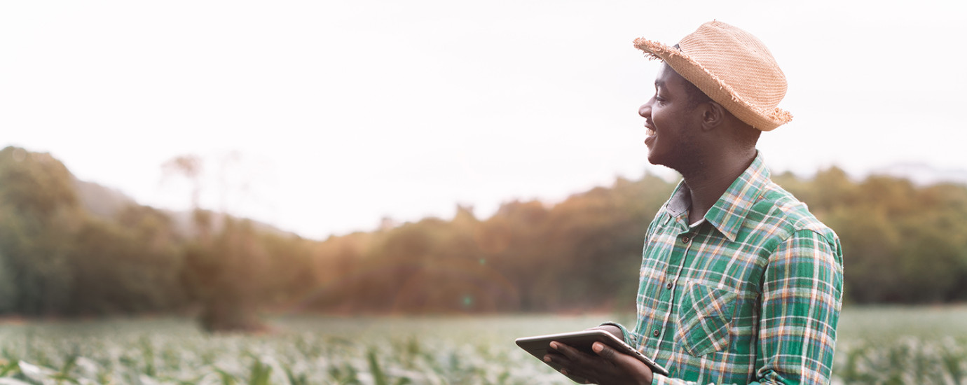 African farmer standing in a field holding a tablet