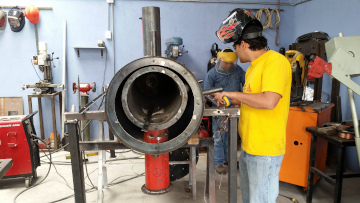 a man standing besides a metal prototype while holding wielding equipment