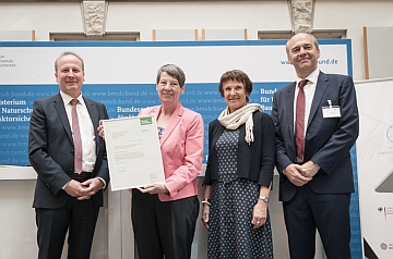 four people standing together while one holds a document towards the camera