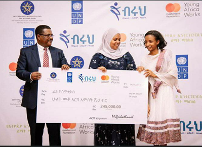 2 diverse persons in festive clothes awarding young female founder from Ethiopia with a check. Wall with sponsor logos in the background