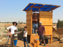 three men and two children in front of a wooden hut