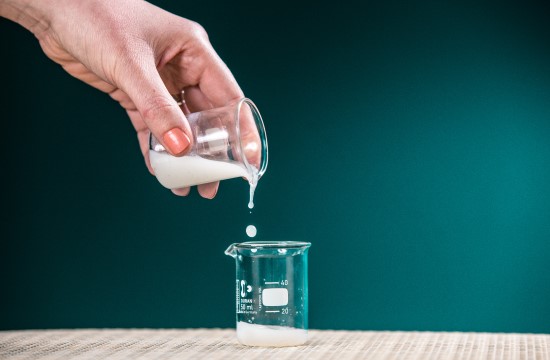 a hand pouring a beaker of opaque white liquid into another beaker