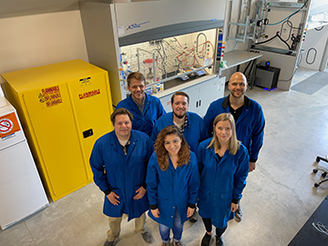 six persons in blue lab coats in a laboratory