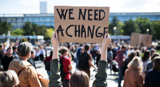 Woman holding a sign stating "We need change"