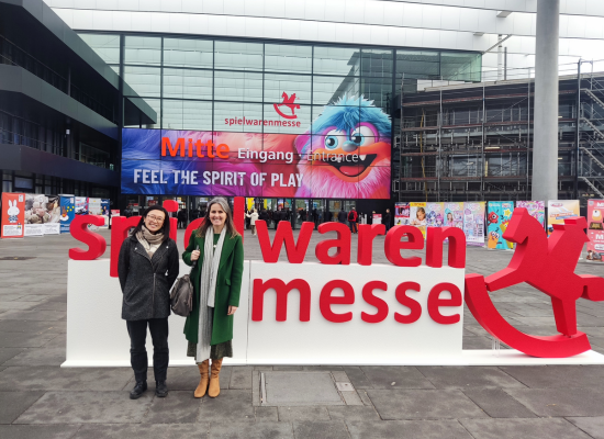 two women standing in front of the toy fair smiling