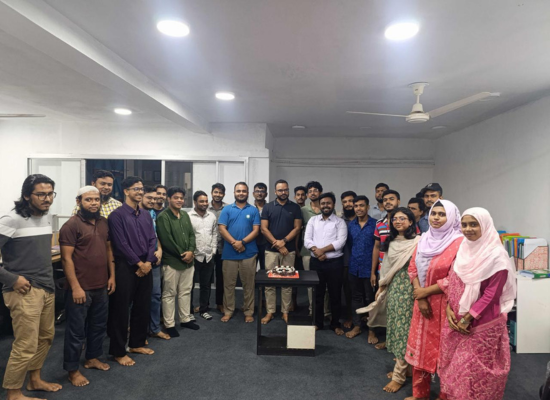 Big group of people standing in an office room in a half-circle, looking into the camera