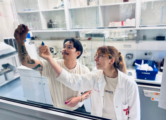 Man and woman drawing on a transparant board in a laboratory setting.