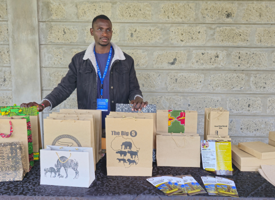 African man standing behind a desk, presenting paper bags and boxes on the desk