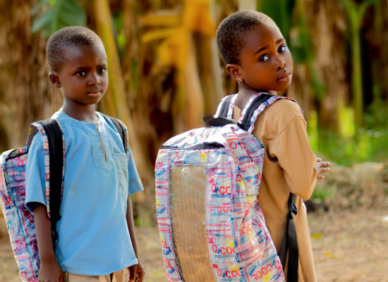 Two african children (approx. 8 years old, one girl, one boy wearing a solar bag, girl looking over her shoulder towards the camera).